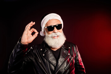 Santa rocker in leather jacket with white beard wears black sunglass and gives the ok gesture in a festive portrait