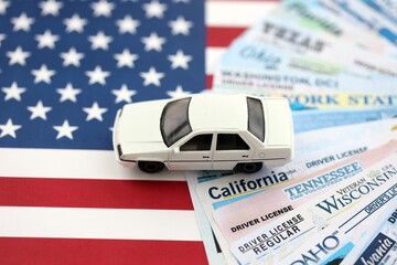 Toy car on big amount of driving licenses from different USA states on flag close up. Stack of driving license specimen cards