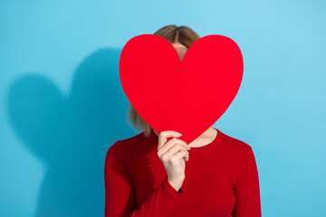 Young woman holding red heart against blue background symbolizing love, warmth, and affection with fashionable style