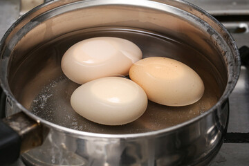 Boiling eggs in pot of water on gas stove. Cooking breakfast food in kitchen. Concept of simplicity, homemade meal, and traditional culinary preparation.