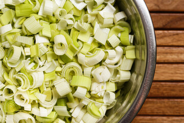 Fresh chopped leek in metal bowl on wooden background. Preparation for cooking healthy meal. Ingredient for soup or salad rich in vitamins and fiber.