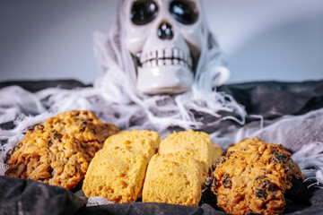A close-up of golden rectangular butter cookies and thick oatmeal raisin cookies arranged on a dark cloth with a net in the background.