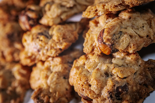 Close-up of chunky oatmeal cookies featuring whole hazelnuts and a golden-brown texture on a white surface. No visible logos or packaging.