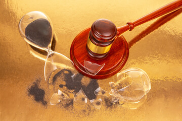 Gavel on shiny surface next to broken hourglass symbolizing lost time and justice