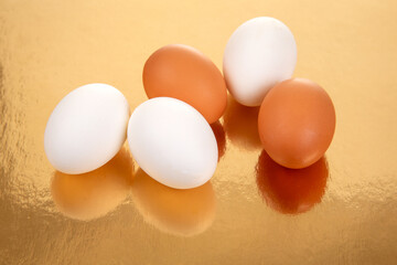 Fresh brown and white eggs arranged on a shiny golden surface in an elegant display