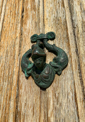Venic, Italy - November 06, 2021: Antique bronze door knocker featuring a unique design of a woman with fish on a rustic wooden door