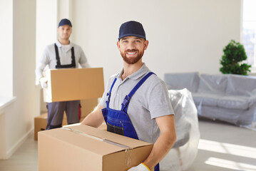 Portrait of positive man mover holding cardboard box during relocation to new home or office, providing moving service and delivery in a professional setting with focus and teamwork.