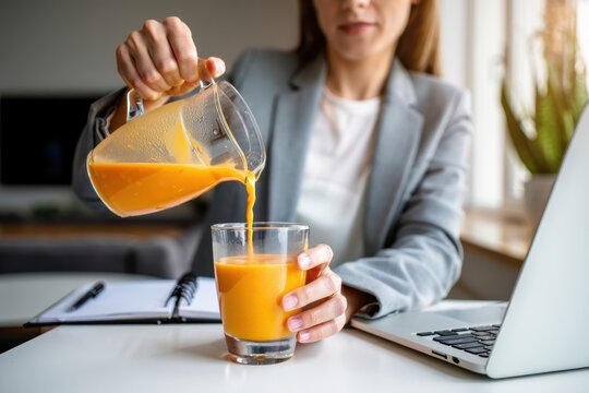 Woman pouring fresh orange juice into a glass at a modern workspace