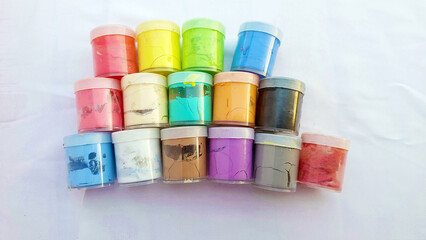 small jars of colorful paint (red, yellow, green, blue, purple, brown, black, white) stacked randomly on a white cloth.