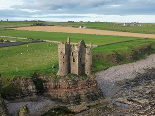 Aerial drone views of Keiss Castle near Wick, reveal its dramatic ruins perched on a rugged cliff...
