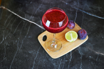 Berry smoothie with plums and a slice of lime on a light background