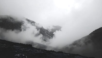 Moody grayscale shot capturing mountain peaks partially obscured by thick fog and low-lying clouds, creating a dramatic, ethereal landscape