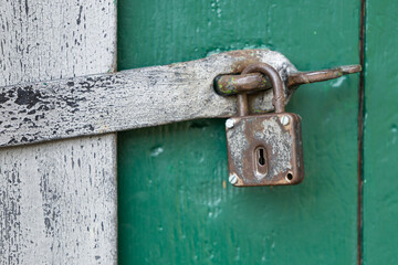 Old rusted padlock securing peeling wooden door