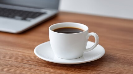 A cup of coffee on a wooden table next to a laptop, evoking a cozy workspace atmosphere.