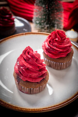 Delicious chocolate cupcakes topped with red buttercream, served on a ceramic plate with a warm festive atmosphere. Perfect sweet dessert for Christmas and New Year celebration.