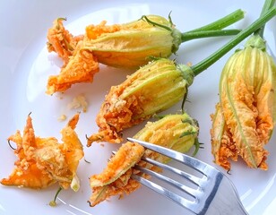 Several deep-fried zucchini flowers on a white plate. A fork is partially visible, indicating someone is about to eat one.