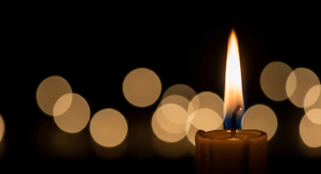 Lit candle with tall flame blue at the base in front of bokeh lights against a dark background