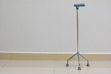 Four-legged walking cane with a blue handle against a white wall.