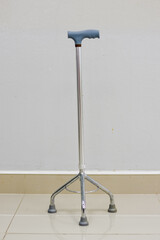 Four-legged walking cane with a blue handle against a white wall.