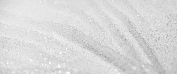 A chic background of white lace textiles with beads and sequins. Folds of fabric for a wedding dress in close-up with a place for text. wedding decor.