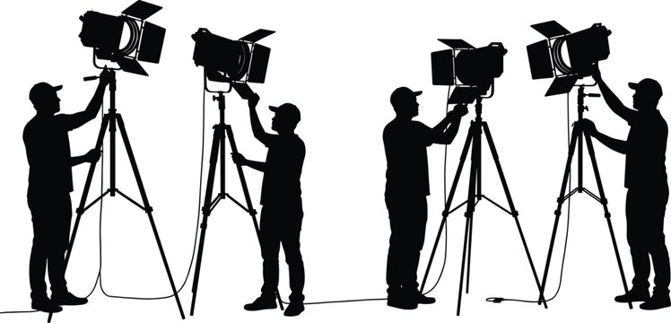 Silhouette of film crew technicians adjusting studio lighting equipment on tripods, professional photographers setting up lights for movie and video production scene
