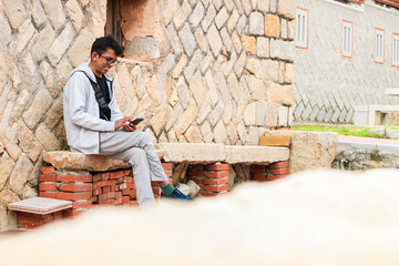 Tourist sitting on a bench smiling and browsing phone in front of a Fujian-style house in Kinmen. Exploring travelling Island of Taiwan, selective focus.