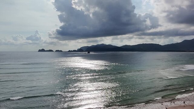 Pantai Pulau Merah or Red Island Beach, Banyuwangi, Indonesia. Tropical waves washing ashore with the iconic forested porphyry island in the background.