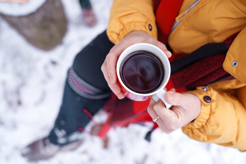 Close-up of hands holding hot beverage in red white mug outdoors in snowy surroundings, evoking warmth and comfort in wintertime. Winter comfort and warmth. Mindful moments
