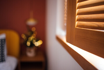 Cozy interior scene featuring wooden window shutters, soft lighting, and a decorative plant with bokeh effect, creating a warm and inviting atmosphere for relaxation and comfort