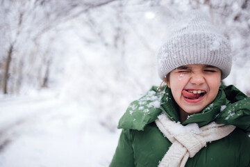 Little girl with a joyful expression, wearing a green winter coat and gray knitted hat, enjoying a snowy landscape, surrounded by frosted trees, capturing the essence of winter fun
