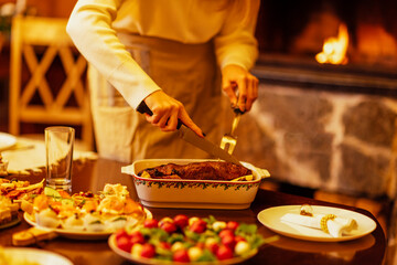 Close-up of a woman cutting a baked duck for a festive dinner. A table with delicious Christmas dishes