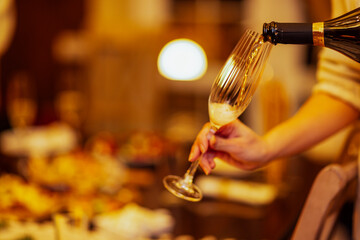 Close-up of a bottle of sparkling wine and a glass. The cup is filled with champagne. A festive table set in the background.