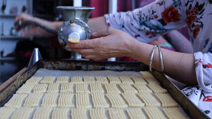 Halwa Lbouq (Moroccan Horn Pastry) - Batch of Sesame-Coated Pastries Ready to Bake, Woman Shaping Raw Dough with Traditional Cookie Press, Silver Bracelets, Home Baking Setup for Eid/Ramadan