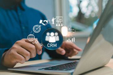 Businessman using laptop with CRM customer relationship management system interface showing marketing icons, data analytics, communication, sales growth, and digital business strategy concept.
