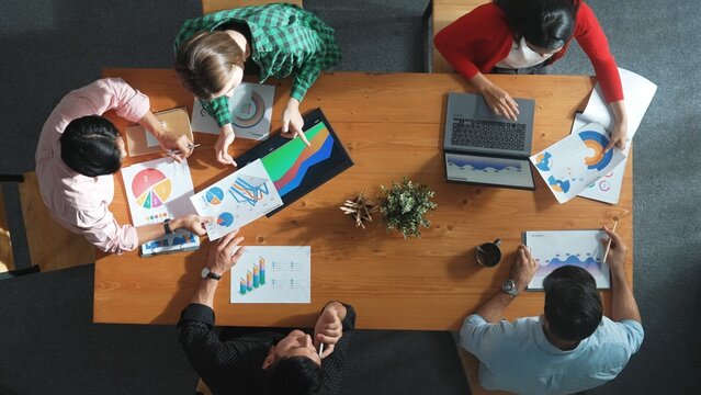 Top down view of business woman explain and present financial chart. Diverse group discuss and listen presentation about stock market statistic at meeting table with investment graph. Convocation. - Powered by Adobe