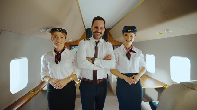 Friendly pilot and two flight attendants smiling at the camera inside a modern private jet, demonstrating excellent service and professionalism for first-class travel and charter flights