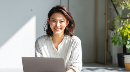 Smiling Japanese woman working on laptop in natural light
