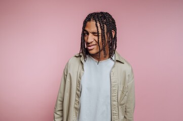 Young man with braided hair winking against pink background.