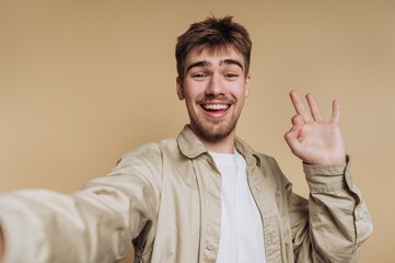 Smiling man taking a selfie against a beige background.