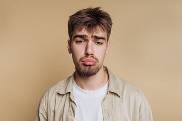 Young man with a sad expression on a beige background.