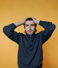 A surprised man with hands on head against an orange background.