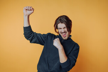 A joyful man celebrating with raised fists against an orange background.