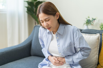 Sick asian young woman in pain, hand holding belly, stomach pain from food poisoning, girl hurt...