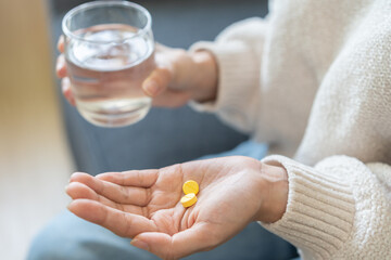 Sick, asian young woman, girl hand holding pill capsule, painkiller medicine from stomach pain, head ache, pain for treatment, take drug or vitamin and glass of water at home, pharmacy and health care