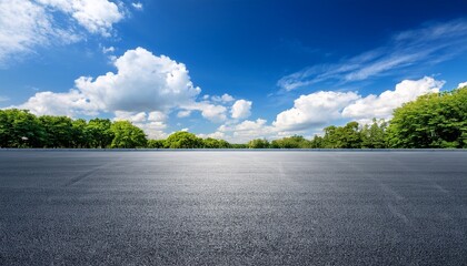 empty asphalt lot under a vibrant blue sky with fluffy clouds and green trees in the background