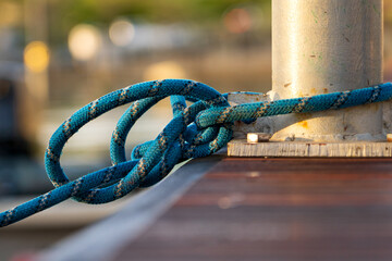 Securely Fastened Blue Rope Wrapped Around Metal Bollard on Wooden Dock, Nautical Knot Holding Boat in Place at Marina