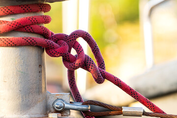 Metal Bollard on Wooden Dock with Red Rope Securely Wrapped, Fastening a Boat in a Rustic Marina Setting with Soft Background