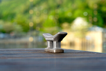 Metal Mooring Cleat on a Wooden Dock, Aged and Weathered, Set Against a Blurred Green Background with Soft Bokeh Lights