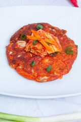 Close-up of Korean kimchi pancake served on a white plate. Traditional Korean food with spicy fermented cabbage topping, showing authentic Asian cuisine and homemade street food concept