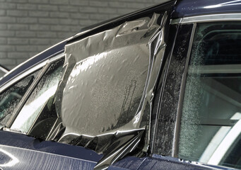 Male car service worker glue window tinting in luxury car detailing car repair the concept of love for cars and protection. Applying tinting foil on a car window in the tuning studio close-up. 